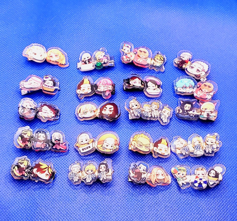 May include: A collection of 20 colorful anime character pins. The pins are made of clear acrylic and feature various characters from popular anime series. The pins are arranged in rows on a blue surface.