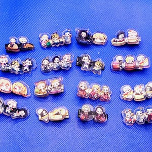 May include: A collection of 18 colorful anime character hair clips. The clips are made of clear plastic and feature various characters from different anime series. Each clip has a different design and color scheme, with some featuring multiple characters.