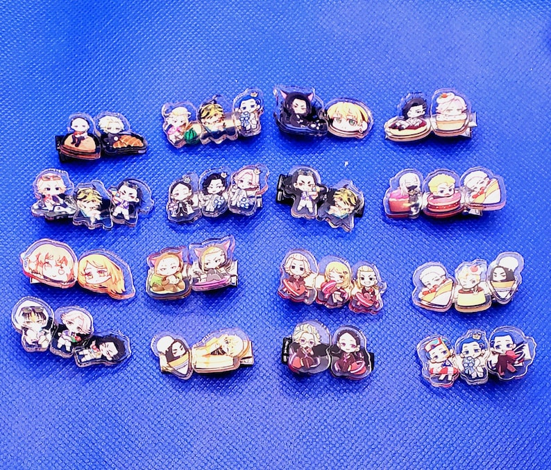 May include: A collection of 18 colorful anime character hair clips. The clips are made of clear plastic and feature various characters from different anime series. Each clip has a different design and color scheme, with some featuring multiple characters.