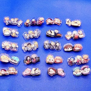 May include: A collection of 20 colorful cartoon character hair clips. The clips are made of clear plastic and feature various characters with different expressions and poses.