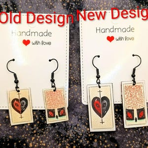 May include: Two pairs of handmade earrings with black hooks. One pair features a heart design, the other a maze. The cards read "Old Design" and "New Design". The cards also read "Handmade with love".