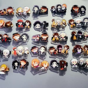 May include: A collection of colorful anime character acrylic charms featuring various characters with different expressions and poses. The charms are displayed on a light gray surface.
