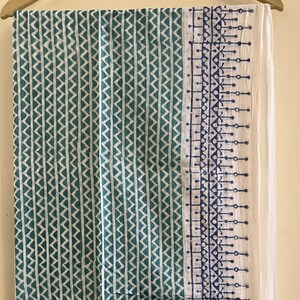 May include: A teal and white cotton fabric with a geometric pattern. The fabric has a white border with a blue and white geometric pattern.