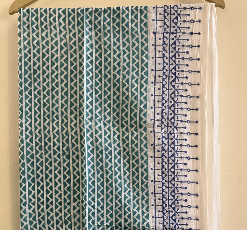 May include: A teal and white cotton fabric with a geometric pattern. The fabric has a white border with a blue and white geometric pattern.