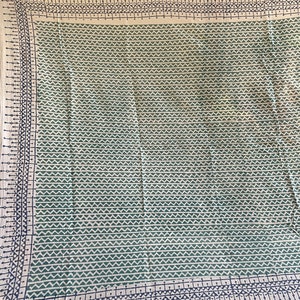 May include: A cream-coloured fabric tablecloth with a green and black geometric pattern. The pattern is a repeating design of small triangles and lines.
