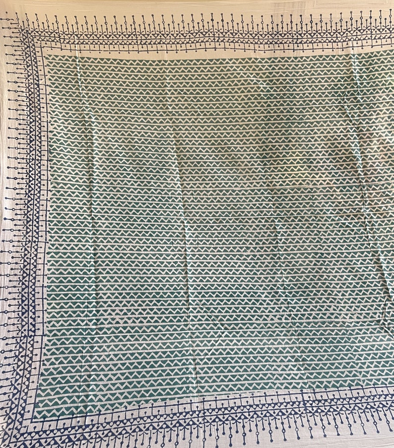 May include: A cream-coloured fabric tablecloth with a green and black geometric pattern. The pattern is a repeating design of small triangles and lines.