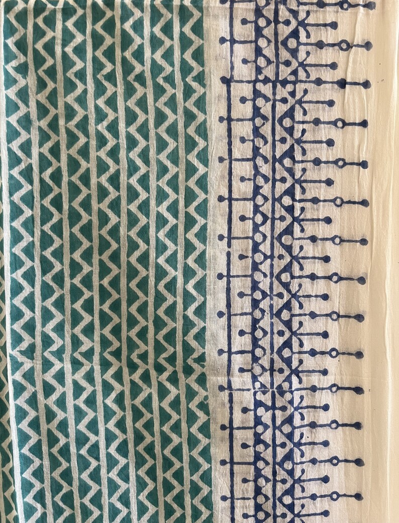 May include: A white fabric with a teal and blue geometric pattern. The fabric has a chevron pattern on the left side and a more intricate pattern on the right side.