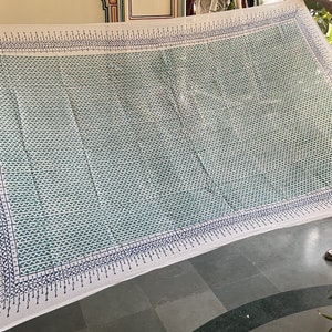 May include: White cotton fabric with a blue and green geometric pattern. The fabric has a border of small blue and white triangles.