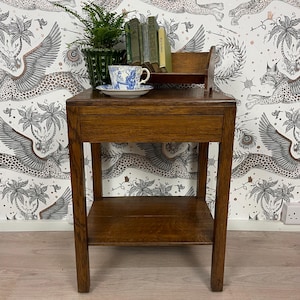 May include: A brown wooden side table with a single drawer and a lower shelf. On top sits a green potted fern, a white and blue patterned teacup and saucer, and a small wooden rack holding four books with visible spines.