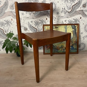 May include: A wooden chair with a curved back and a square seat. The chair is made of warm brown wood and has four straight legs. The chair is positioned in front of patterned wallpaper and a framed picture.