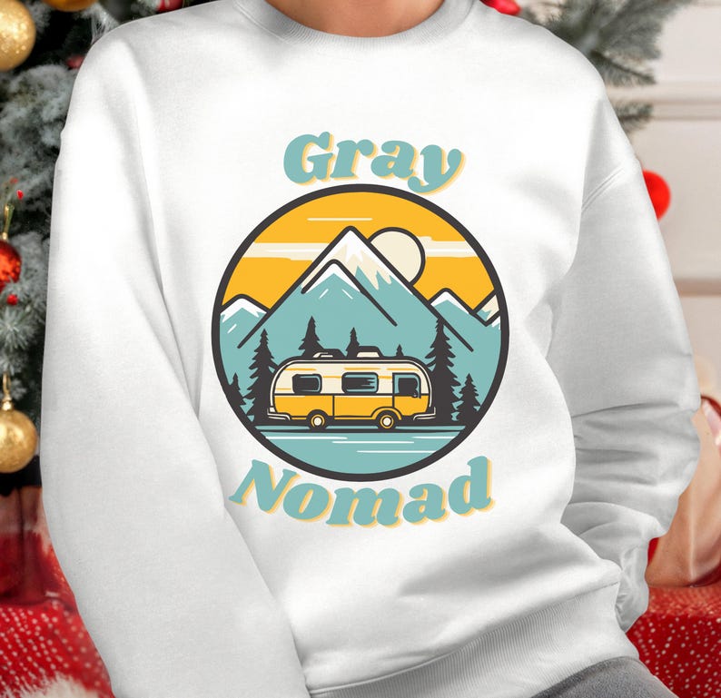 K&ouml;nnte beinhalten: Wei&szlig;er Pullover mit einem Retro-Grafikdesign. Das Design zeigt einen gelben Wohnwagen vor einer Berglandschaft mit Sonnenuntergang. Der Text "Gray Nomad" ist in einer Retro-Schriftart geschrieben.
