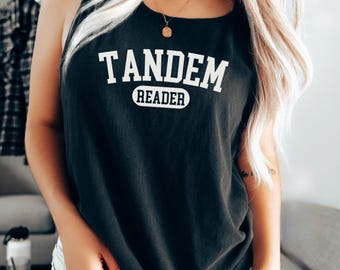 May include: Black tank top with the text "TANDEM READER" in white block letters. The word "READER" is in a white oval. The tank top is sleeveless and has a scoop neck.