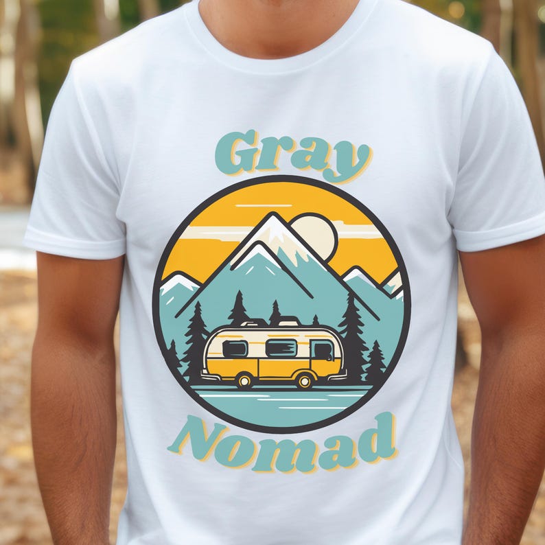 Peut inclure: T-shirt blanc avec un graphique d'un camping-car jaune devant une cha&icirc;ne de montagnes bleues avec un soleil jaune et le texte "Gray Nomad" en bleu et jaune.