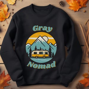 K&ouml;nnte beinhalten: Schwarzes Sweatshirt mit einer Retro-Illustration eines Wohnmobils vor Bergen. Der Text "Gray Nomad" ist in einer Retro-Schrift gedruckt.