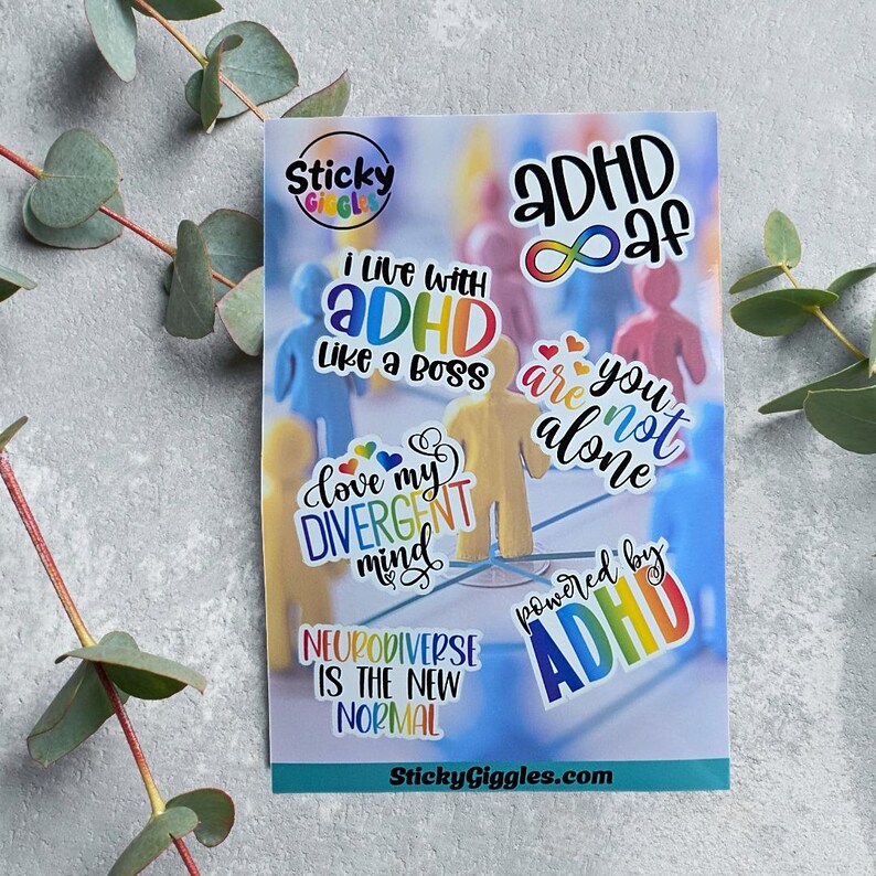 Puede incluir: Una hoja de pegatinas coloridas con frases relacionadas con el TDAH y la neurodiversidad. Las pegatinas incluyen texto como "ADHD AF", "I live with ADHD like a boss" y "Neurodiverse is the new normal". El fondo presenta figuras borrosas.
