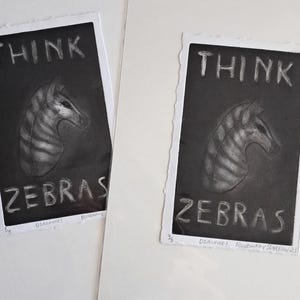 May include: Two framed art prints with the words "THINK ZEBRA" above a zebra head illustration. The prints are black and white with a textured appearance, and the edges are uneven.