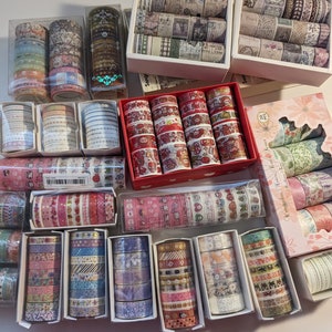May include: Assortment of colorful washi tape rolls in various patterns and designs. The washi tape is packaged in clear plastic boxes and red, white, and blue boxes.