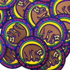 May include: Circular embroidered patches featuring a brown sloth hanging from a branch. The patches have a yellow and green inner circle, a blue outer ring with the text "Come waste your time with me," and purple accents.