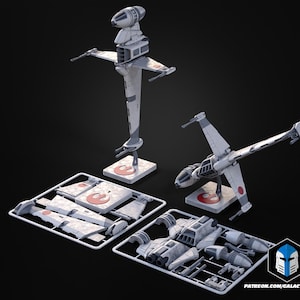 May include: A model kit of a Star Wars B-wing starfighter, with two assembled models and unassembled parts. The models are light gray with red and white accents. The kit includes a stand with a red symbol.
