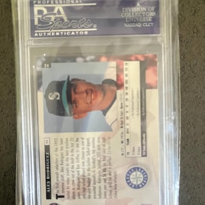 May include: A baseball card of Alex Rodriguez, graded and encased in a protective holder. The card features a photo of Rodriguez in a Seattle Mariners uniform. The card is labeled with "PSA Sports Authenticator."