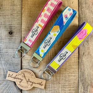 May include: Three colorful keychains with different patterns. The keychains are made of fabric and have a metal ring. The keychains are handmade by Blueberry Bagworks in Minnesota.