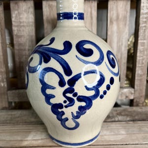 May include: A white ceramic bottle with a blue and white design. The bottle has a round body and a narrow neck. The design features a floral pattern with swirls and dots.