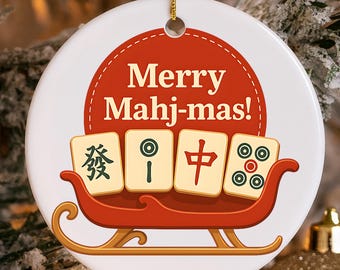 May include: A white ceramic Christmas ornament with the text "Merry Mahj-mas!" in red. The ornament features a red sleigh carrying four Mahjong tiles. A gold string is attached for hanging.