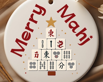 May include: A white ceramic ornament with the words "Merry Mahj" in red script. A Christmas tree is formed from Mahjong tiles, with a gold star at the top. A brown string is attached for hanging.