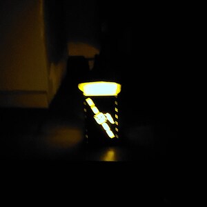 May include: A black and white striped box with a yellow light shining through the front. The box is sitting on a dark surface.