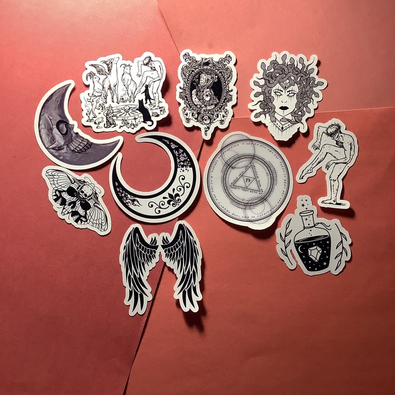 Puede incluir: Una colecci&oacute;n de pegatinas con temas g&oacute;ticos y m&iacute;sticos. Los dise&ntilde;os incluyen una luna calav&eacute;rica, una polilla, una luna creciente, alas de &aacute;ngel, Medusa, una botella de poci&oacute;n y otras ilustraciones en blanco y negro.