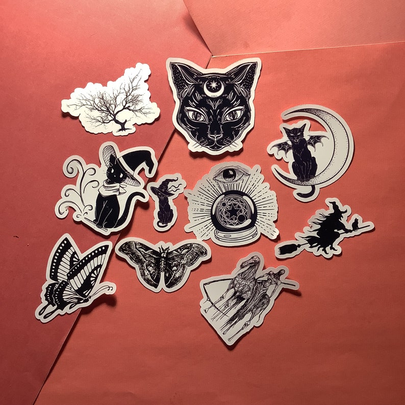 Puede incluir: Una colecci&oacute;n de pegatinas en blanco y negro con tem&aacute;tica m&iacute;stica. Los dise&ntilde;os incluyen un gato negro con una luna creciente, una bruja en una escoba, una mariposa, un &aacute;rbol, una bola de cristal y un gato en una luna creciente.