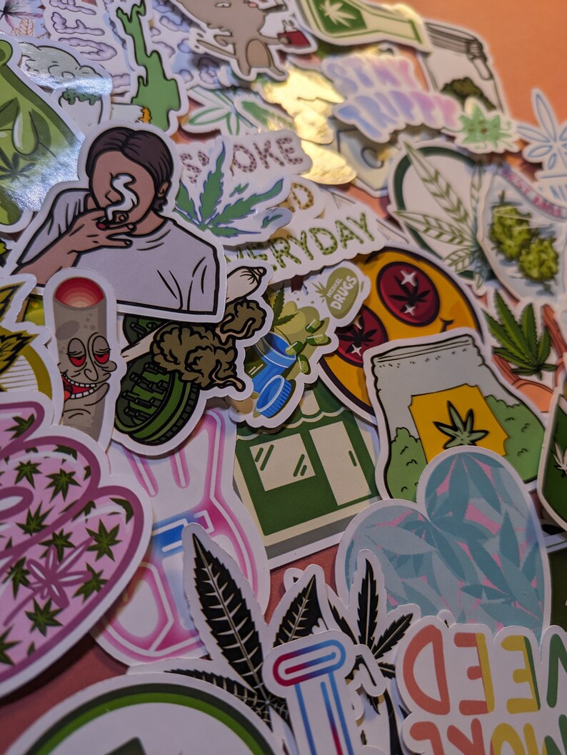 May include: A collection of colorful stickers with cannabis-related designs. The stickers feature illustrations of marijuana leaves, smoking figures, and text like "Smoke Everyday" and "More Weed". The stickers are in various shapes and sizes.