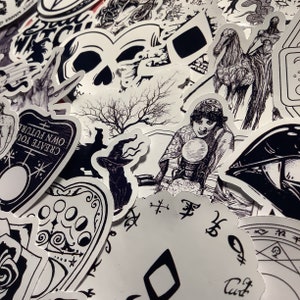 Puede incluir: Una colecci&oacute;n de pegatinas en blanco y negro con temas ocultos y g&oacute;ticos. Los dise&ntilde;os incluyen una calavera, una bruja con sombrero, una adivina con una bola de cristal y una tabla Ouija. Las pegatinas son de varias formas y tama&ntilde;os.