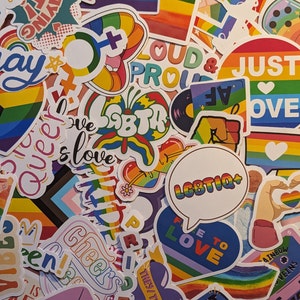 May include: A selection of LGBTQ+ pride stickers in various colours. The stickers display rainbows, hearts, and phrases such as "Love," "Queer," and "Just Love." Some stickers have the text "LGBTIQ+" and "Free to Love."