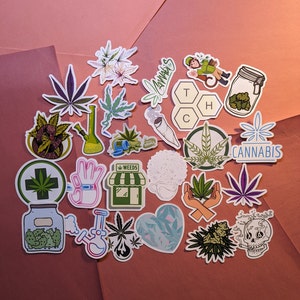 May include: A collection of colorful cannabis-themed stickers. Designs include marijuana leaves, bongs, a jar of buds, and the word "Cannabis". The stickers are arranged on a pink and brown background.