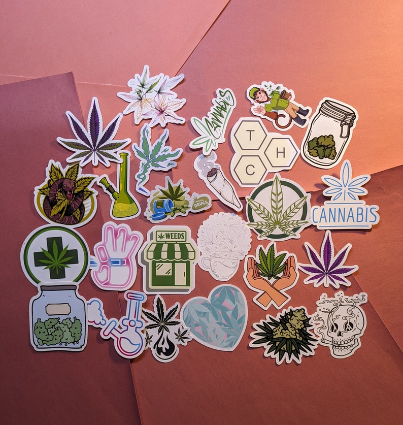 May include: A collection of colorful cannabis-themed stickers. Designs include marijuana leaves, bongs, a jar of buds, and the word "Cannabis". The stickers are arranged on a pink and brown background.