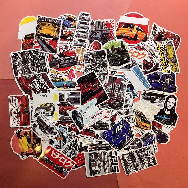 May include: A collection of colorful car-themed stickers. The stickers feature various car illustrations, Japanese text, and graphic designs. The color palette includes red, yellow, blue, and black. Some stickers have the text "GODZILLA" and "ROUGH WORLD".