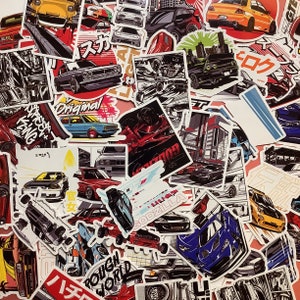 Może przedstawiać: Kolekcja naklejek o tematyce samochodowej o różnych wzorach i kolorach. Naklejki przedstawiają ilustracje klasycznych i nowoczesnych samochodów, a także japoński tekst i elementy graficzne. Niektóre naklejki mają tekst "GODZILLA" i "ROUGH WORLD".