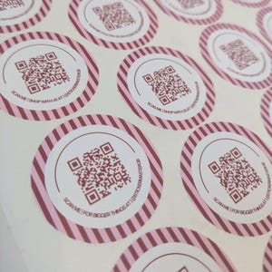 May include: A sheet of circular stickers featuring a central QR code surrounded by a white border and a pink and white striped edge. The text SCAN ME | SHOP WITH US AT | @STICKERMASTERGB or SCAN ME | FOR BIGGER THINGS AT | @STICKERMASTERGB is printed.