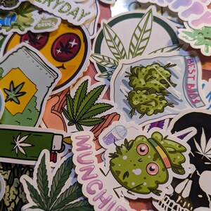 May include: A collection of colorful stickers featuring cannabis-related designs. Stickers include images of marijuana leaves, buds, and cartoon characters. Text includes "Munchies", "Best Buds", and "Stay Trippy".