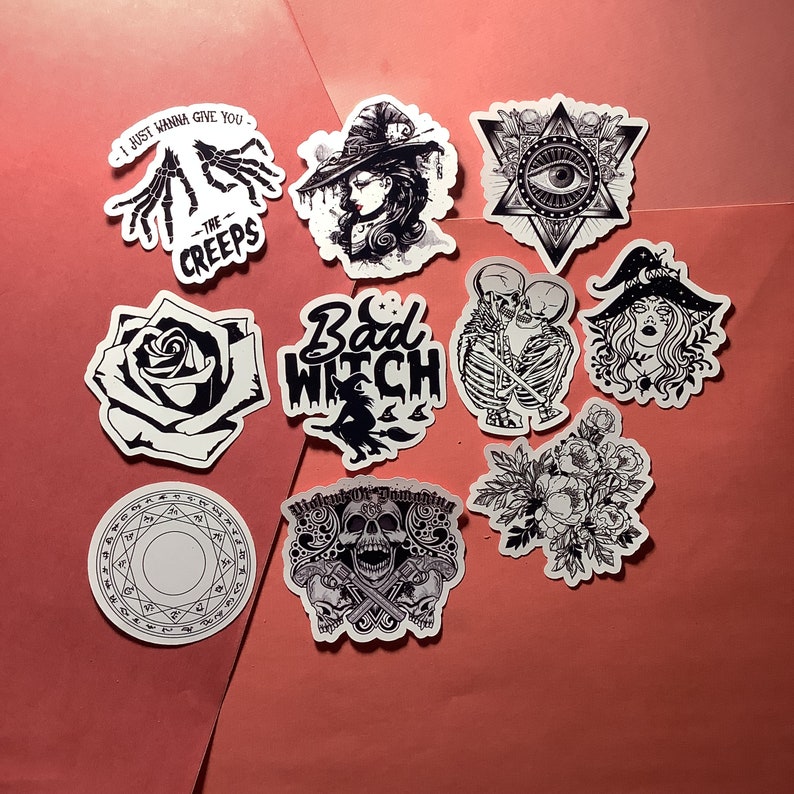 Puede incluir: Una colecci&oacute;n de pegatinas en blanco y negro con temas g&oacute;ticos y de brujas. Los dise&ntilde;os incluyen una bruja, esqueletos, rosas, un ojo dentro de una estrella y los textos "Bad Witch" y "I just wanna give you the creeps".