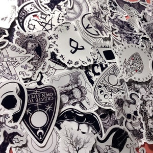 Puede incluir: Una colecci&oacute;n de pegatinas en blanco y negro con temas ocultos y g&oacute;ticos. Los dise&ntilde;os incluyen calaveras, tableros Ouija, lunas y texto que dice "CREATE YOUR OWN FUTURE". Las pegatinas son de varias formas y tama&ntilde;os.