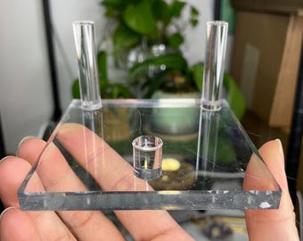 May include: A clear acrylic display stand with two vertical posts and a circular base. The stand is designed to hold and display small objects.