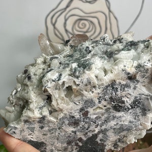 May include: A large, grey and white crystal cluster with a few pink crystals. The crystal has a rough, textured surface.