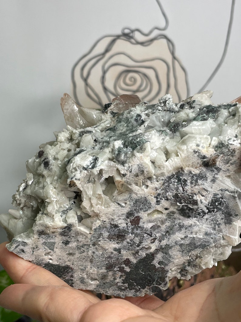 May include: A large, grey and white crystal cluster with a few pink crystals. The crystal has a rough, textured surface.