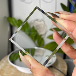 Könnte beinhalten: Ein quadratischer Glasprisma, auch bekannt als Kristall, wird in einer Hand gehalten. Das Prisma ist glatt und reflektierend.