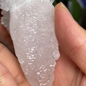 Op de afbeelding: Een witte, doorschijnende kristalkluster met een ruw, getextureerd oppervlak. De kristal is traanvormig en heeft veel kleine, puntige kristallen.