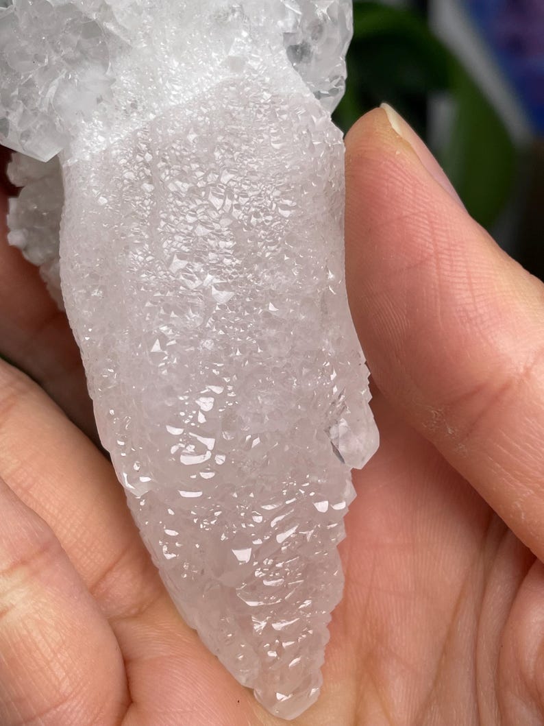 Op de afbeelding: Een witte, doorschijnende kristalkluster met een ruw, getextureerd oppervlak. De kristal is traanvormig en heeft veel kleine, puntige kristallen.