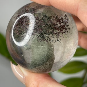 May include: A clear quartz sphere with green and black inclusions. The sphere has a white ring around the center.