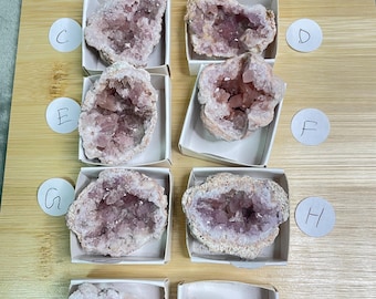 May include: Ten small boxes each containing a pink amethyst geode. The boxes are labeled with letters A through J.